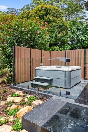 A modern outdoor hot tub with a wooden fence and steps leading up to it, surrounded by a landscaped garden with rocks and plants. - Yume House Stylish Country Escape 1 Bedroom (Ravensbourne)