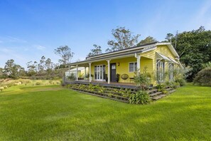 A yellow house with a porch, surrounded by a grassy yard and trees. - The Quince Cottage -  1 Bedroom (Ravensbourne)