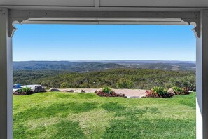 A view from a covered outdoor area with a clear sky, a grassy lawn, and a distant landscape of hills and trees. - The Quince Cottage -  1 Bedroom (Ravensbourne)
