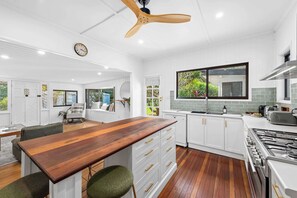 A modern kitchen with white cabinetry, a wooden dining table, and a built-in stove. - Mahali House - 4 Bedroom Holiday House (Ravensbourne)