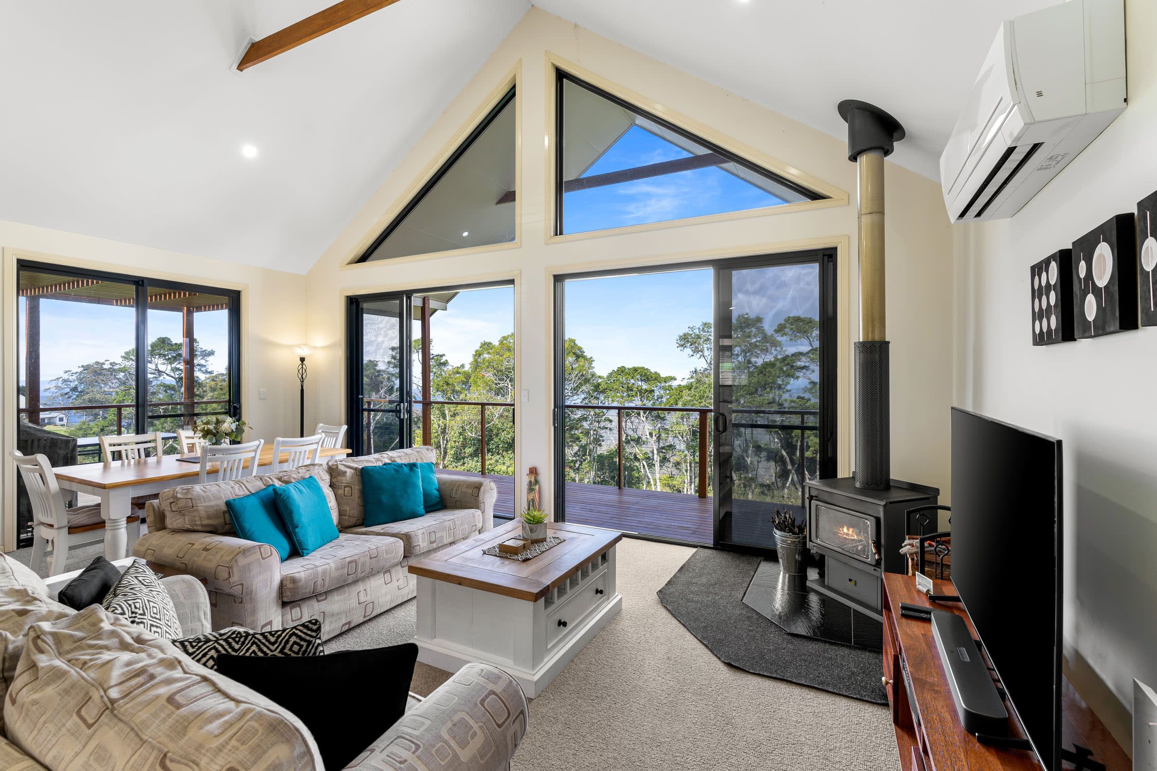 A spacious living area with a high ceiling, large windows, a fireplace, and a dining area with a view.