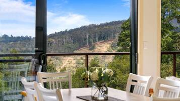 Un coin repas avec une table et des chaises, un vase rempli de fleurs et une vue sur une colline boisée.