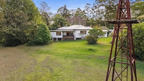 A single-story house with a front porch, surrounded by a well-maintained lawn and dense trees. - Mahali House - 5 Bedroom Holiday House (Ravensbourne)