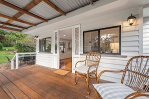 A covered porch with wooden flooring, two wicker chairs, and a table. - Mahali House - 5 Bedroom Holiday House (Ravensbourne)