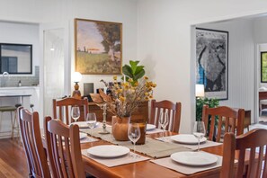 A dining table set for four with chairs, a vase of dried flowers, and candles. - Mahali House - 5 Bedroom Holiday House (Ravensbourne)