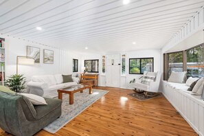 A modern living room with a white sofa, a coffee table, and a bookshelf. - Mahali House - 5 Bedroom Holiday House (Ravensbourne)