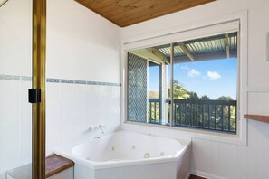 Une salle de bain dotée d’une grande baignoire, d’une fenêtre donnant sur une terrasse en bois et d’un mur carrelé.