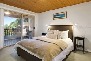 Une chambre avec un grand lit, une table de chevet, une lampe et une vue sur une terrasse extérieure, accessible par une porte vitrée.