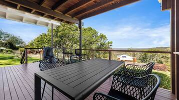 Une terrasse extérieure avec une table et des chaises, donnant sur un jardin aménagé et sur des collines lointaines.