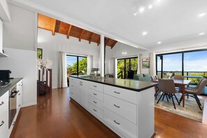 A modern kitchen with a large island, white cabinetry, and a dining area with a view. - Havenwood Chalet 1 Bedroom (Ravensbourne)