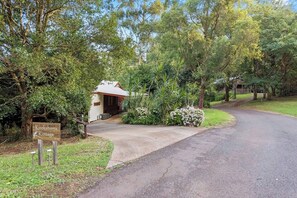 A Kookaburra Cottage with a paved driveway leading to a wooden door, surrounded by lush greenery and trees. - Kookaburra Kottage Luxury Chalet 1 Bedroom (Ravensbourne)