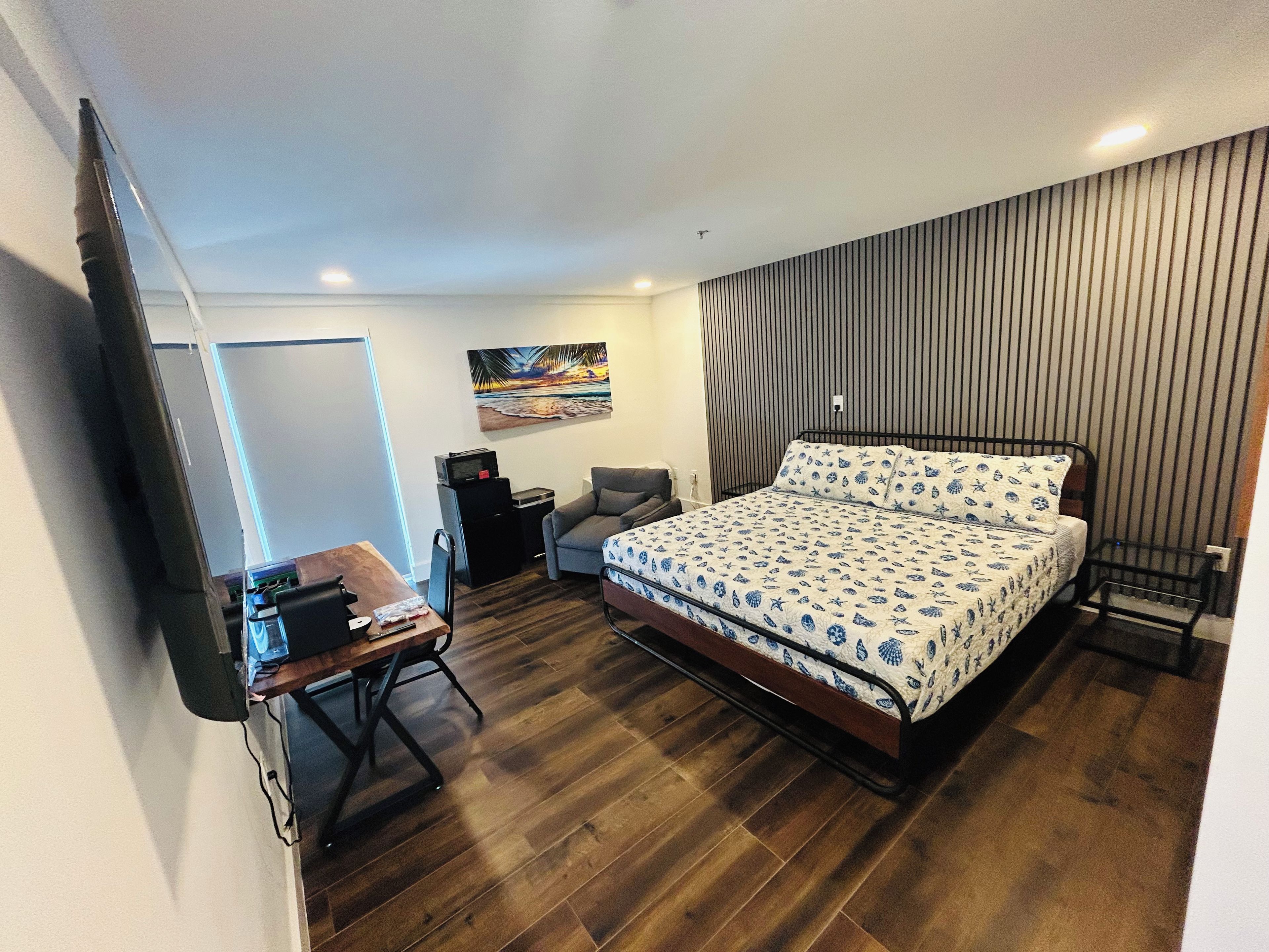 Una habitación de hotel con una cama, un escritorio, una silla, un televisor y un cuadro en la pared.