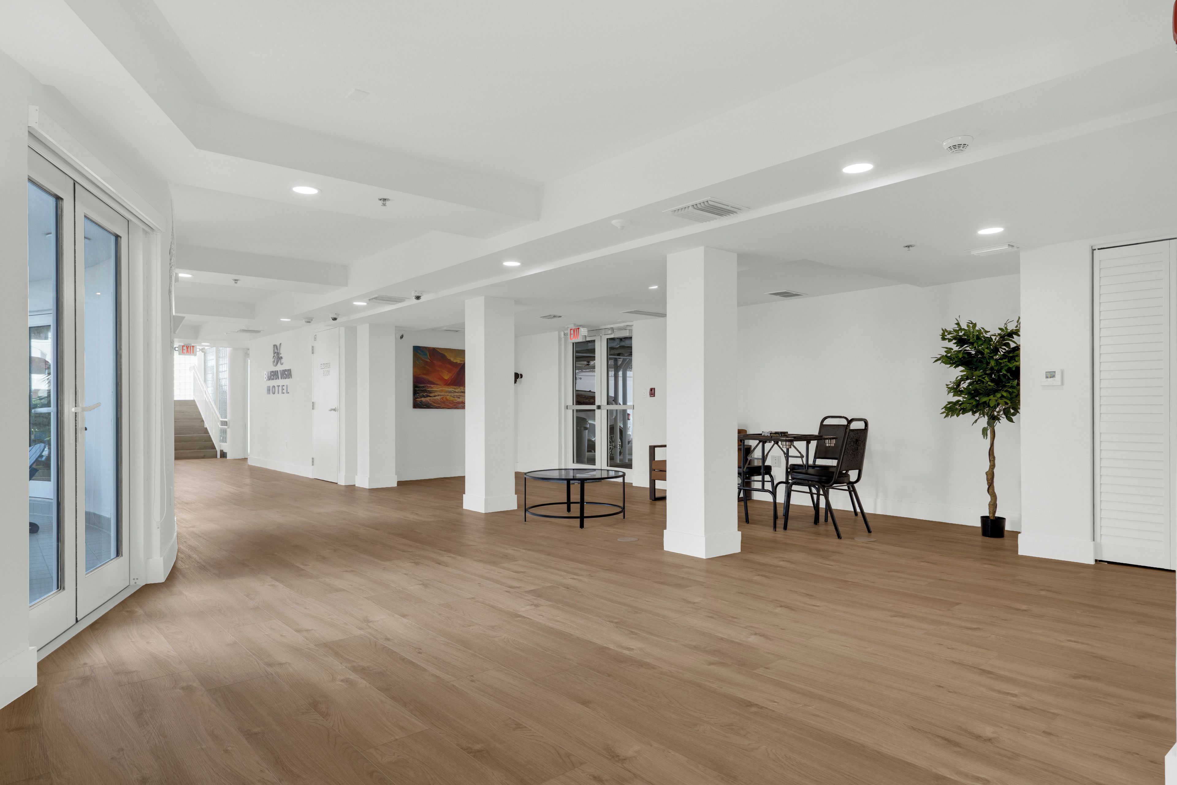 A hotel lobby with a wooden floor, glass doors, a staircase, and a table with chairs.