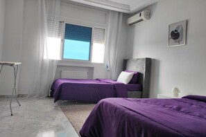 A bedroom with two beds, a radiator, a window with blinds, and a wall-mounted air conditioner. - Urban Flat near Lake (Tunis)
