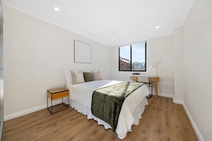 A bedroom with a bed, bedside table, lamp, and a window with a view. - BOWIE - Pyrmont Paradise | Leafy Balcony With City Glimpses (Pyrmont)