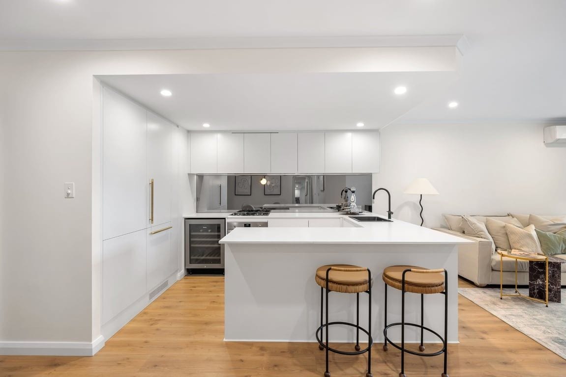 Een moderne keuken met witte kastjes, een centraal eiland en twee krukken.