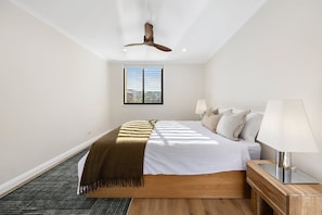 Ein Schlafzimmer mit Bett, Deckenventilator, Fenster und Nachttisch mit Lampe.