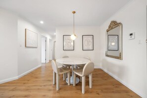 Un comedor con una mesa redonda y sillas, una lámpara colgante, obras de arte enmarcadas en las paredes y un espejo con un marco ornamentado.