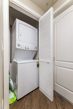 A laundry room with a front-loading washer and dryer, a door with horizontal slats, and a wooden floor. - Charming 2-bedroom apartment with pool, gym and free parking in Marina del Rey! (Marina del Rey)