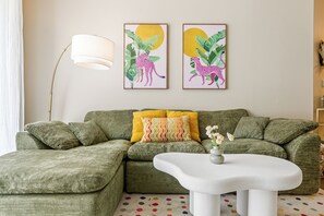 A living room with a green sectional sofa, a white coffee table, and two framed animal prints on the wall. - Charming 2-bedroom apartment with pool, gym and free parking in Marina del Rey! (Marina del Rey)