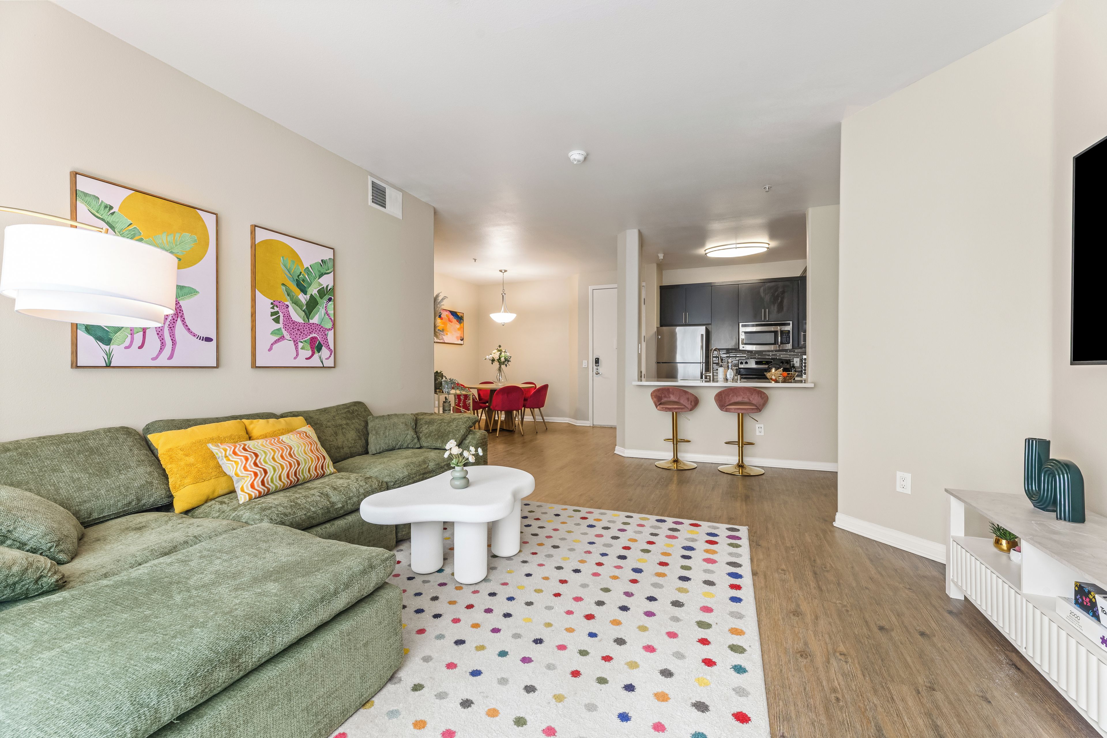 Ein modernes Wohnzimmer mit einem grünen Sofa, einem weißen Couchtisch und einem bunten Teppich mit Punkten.
