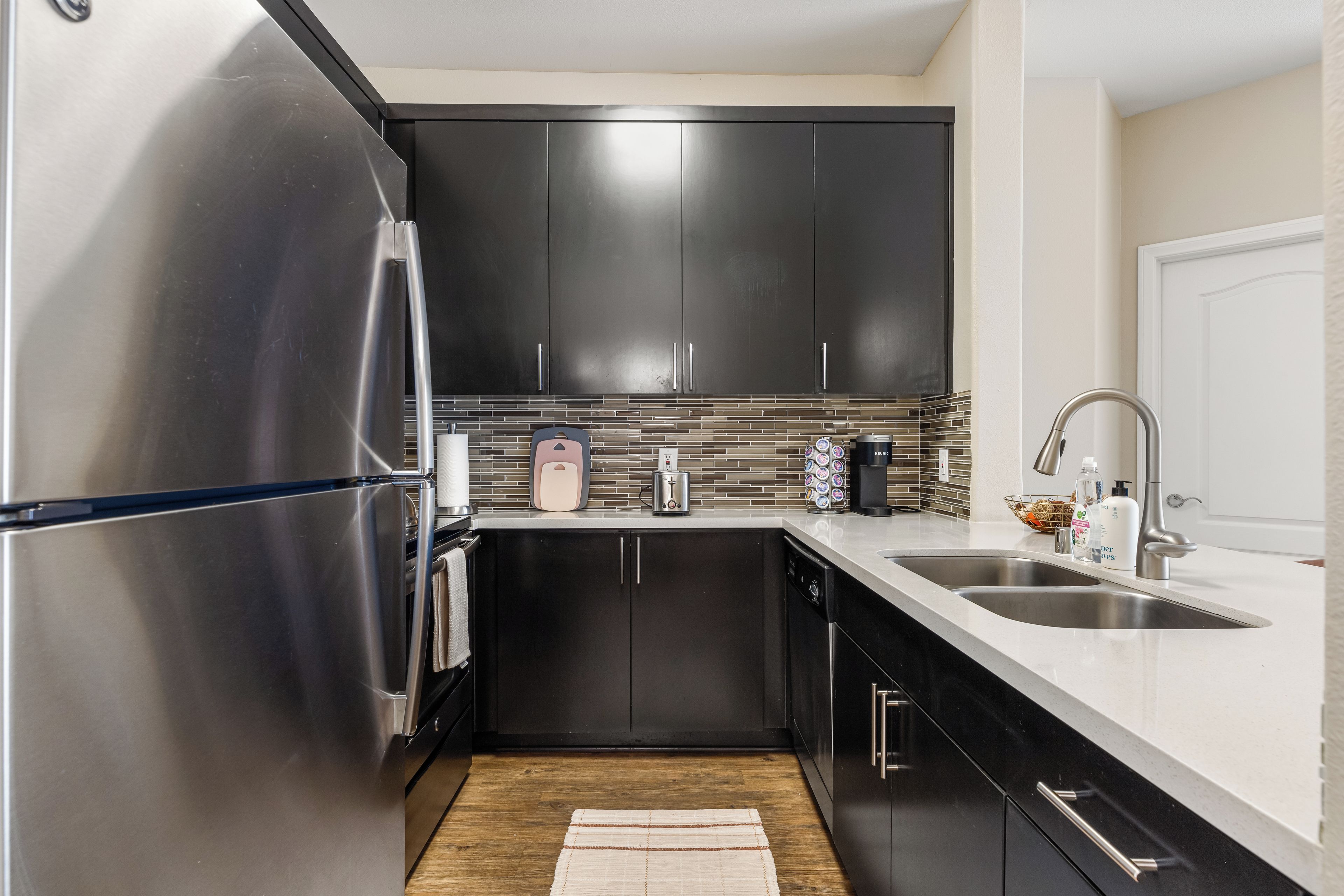 A compact kitchen with stainless steel appliances, dark cabinetry, and a tiled backsplash.