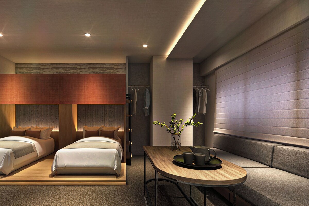 Ein modernes Hotelzimmer mit zwei Betten, einem Holztisch mit Tablett und einer Topfpflanze.