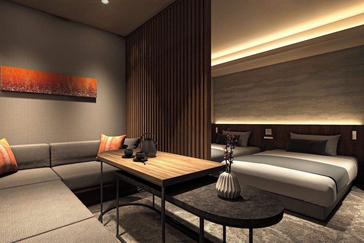A modern hotel room with a sofa, a small table, a bed, and a decorative wall piece.