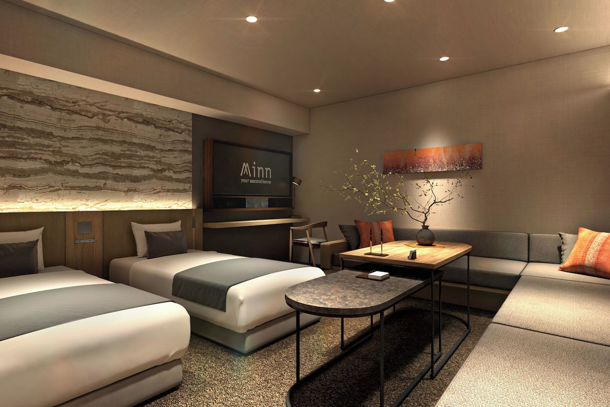 A modern hotel room with two beds, a sofa, a dining table, and a decorative wall.