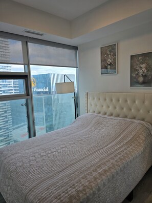 A bedroom with a large bed, a window with blinds, a wall-mounted lamp, and two floral paintings. - Toronto in the Sky | CN Tower & Lake Views (Toronto)