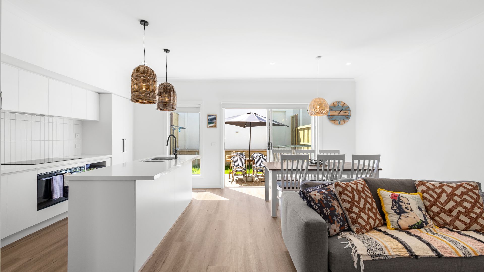 A modern kitchen with white cabinetry, a central island, and two hanging wicker pendant lights.