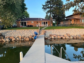 A house with a dock leading to a pond, surrounded by a stone wall and trees. - Sand Lake Extended Stay Ranch - Fully Furnished Lake Home - Monthly Stays (Lindenhurst)