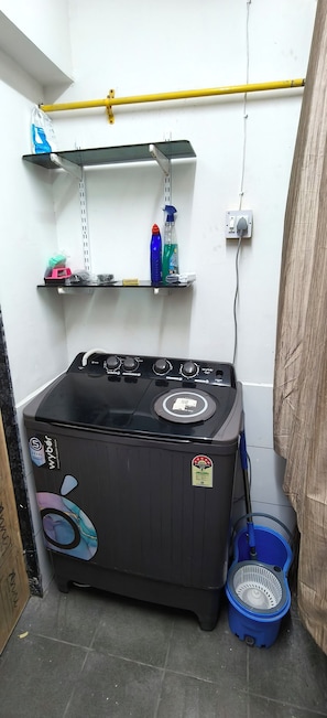 Un kitchenette pequeño con estufa a gas, lavadora azul y un cubo azul.