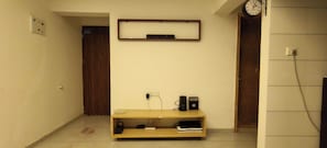 A hallway with a wooden door, a clock, and a shelf with books and electronic devices.