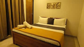 Quarto de hotel com cama, cabeceira de madeira, janela com cortinas e três quadros pendurados na parede.
