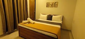 A hotel room with a bed, a wooden headboard, a window with curtains, and three wall-mounted paintings.