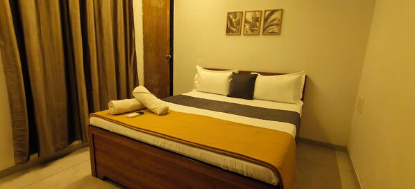 A hotel room with a bed, a wooden headboard, a window with curtains, and three wall-mounted paintings.