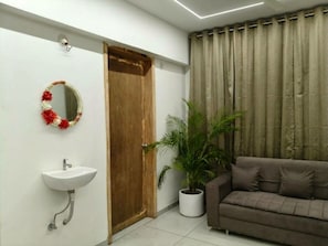 Una habitación con una puerta de madera, un lavamanos blanco, un sofá marrón y una planta en maceta.