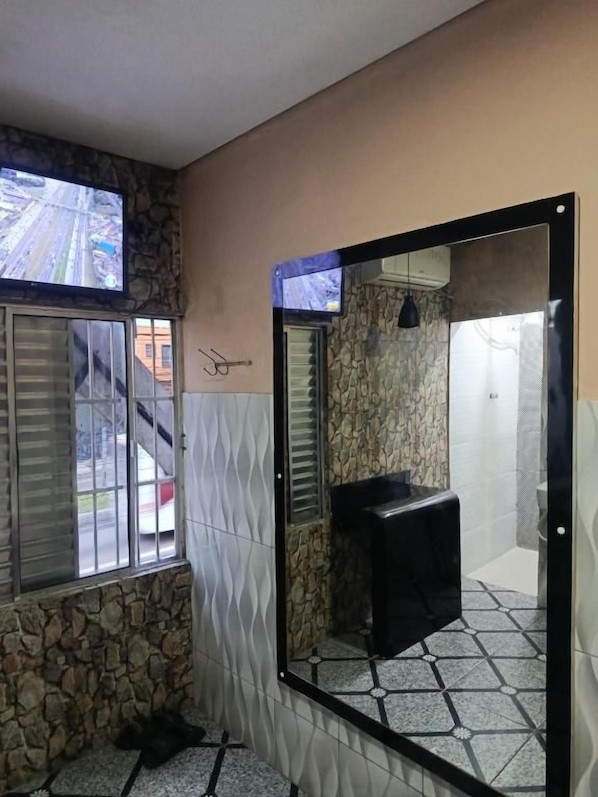 A bathroom with a stone wall, a tiled floor, a black sink, and a window with blinds. - Hotel Santo amaro inn (São Paulo)