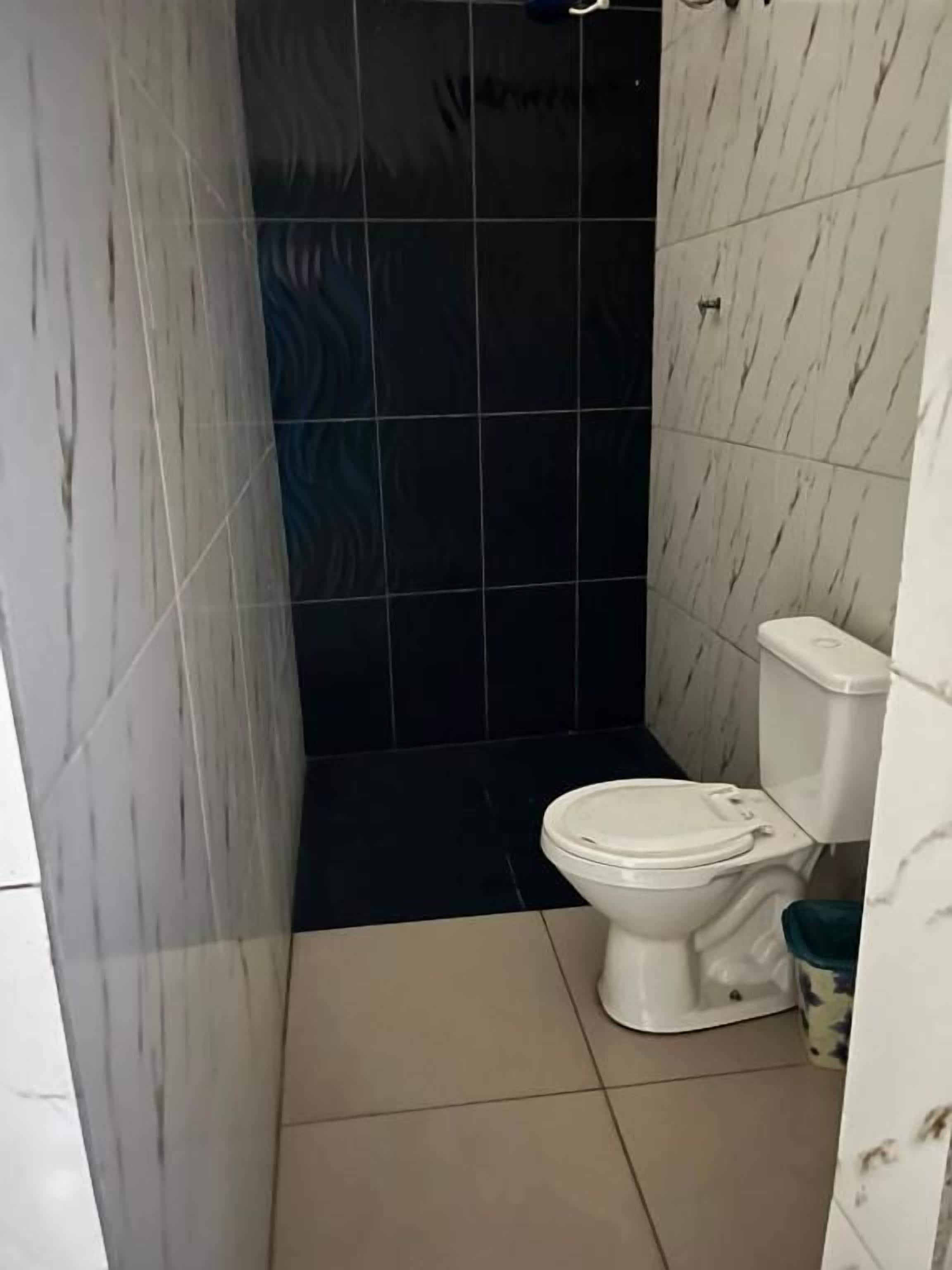 Een badkamer met een toilet, een douche en een betegelde vloer.