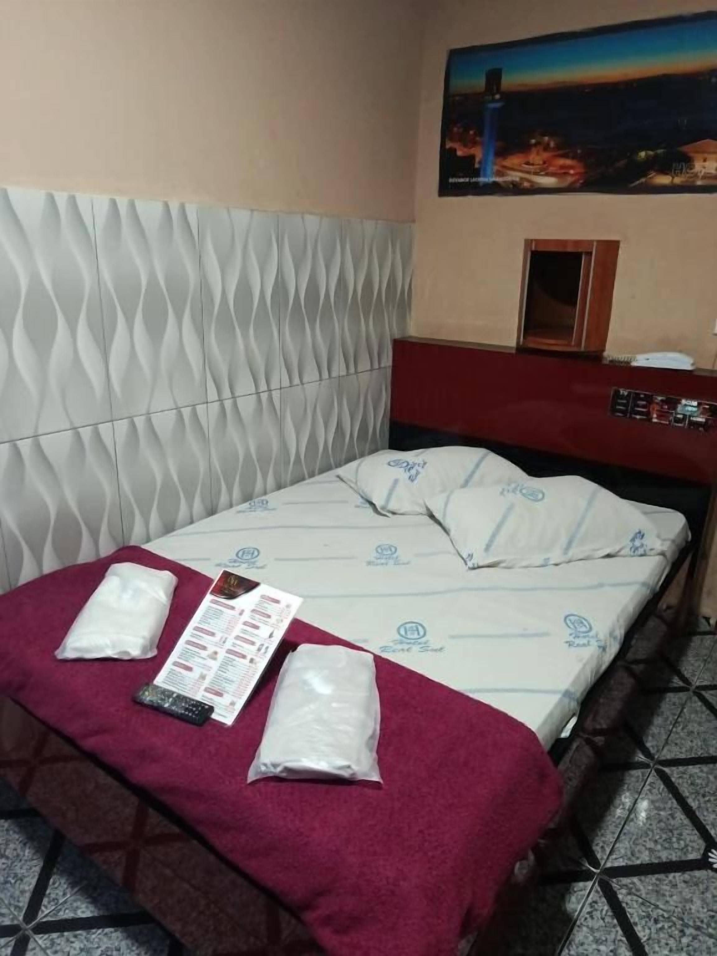 A hotel room with a bed, a red towel, a remote control, and a menu on the bed.