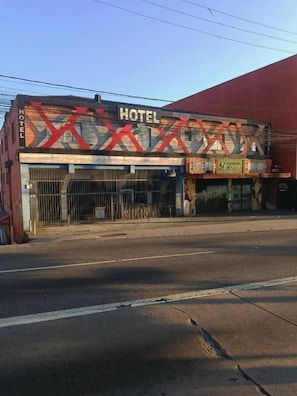 Un hotel con un letrero llamativo, entrada protegida por una reja y toldo rojo.