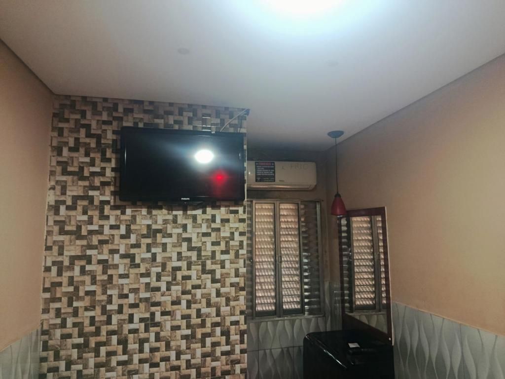 A room with a patterned wall, a flat-screen TV mounted above a window, and an air conditioning unit.