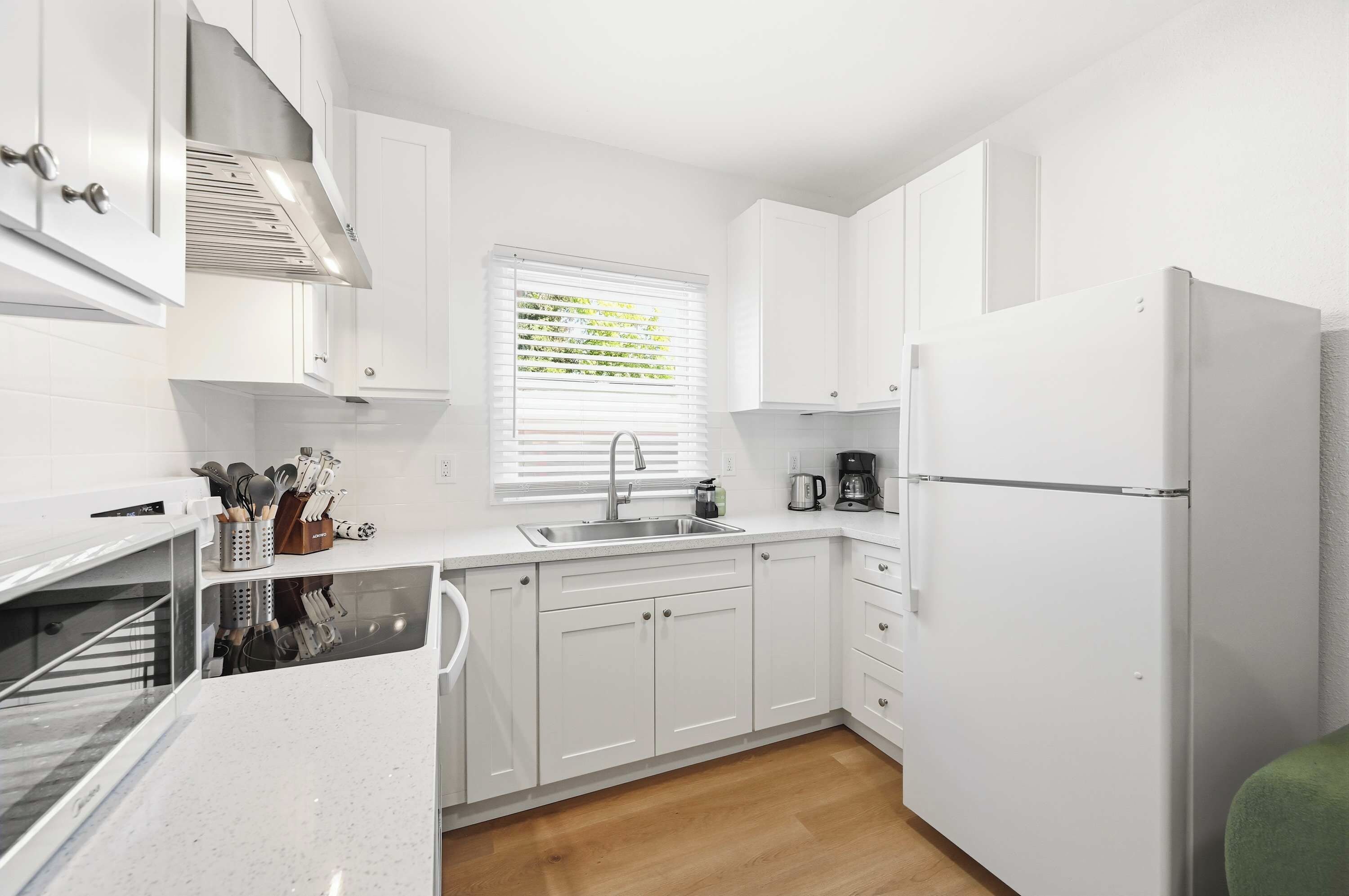 A compact kitchen with white cabinetry, a built-in oven, a sink, and a refrigerator.