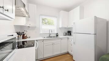 A compact kitchen with white cabinetry, a built-in oven, a sink, and a refrigerator.