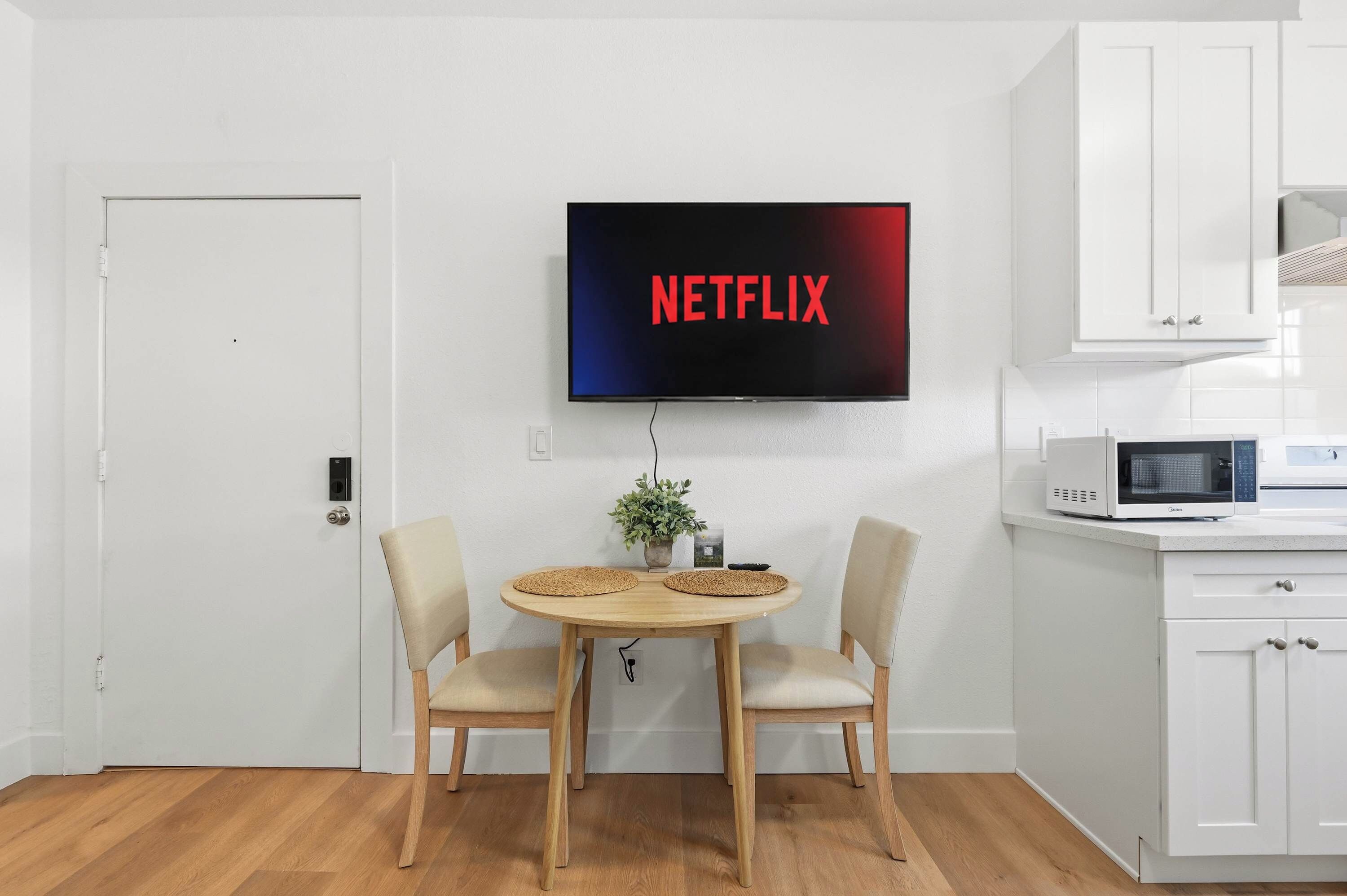 A modern kitchen with a flat-screen TV mounted on the wall displaying 'NETFLIX'.