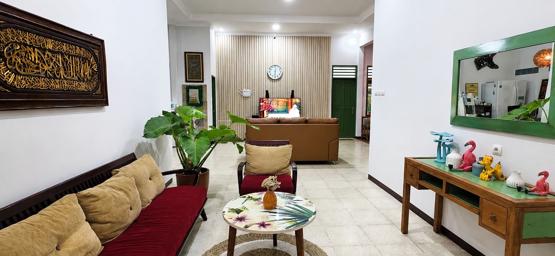 A living room with a sofa, a coffee table, a plant, and a television in the background.