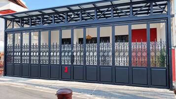 A gated entrance with a metal fence and a red door, number 3 on the gate, and a building with a red shutter visible through the fence.