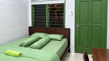 Ein Schlafzimmer mit einem Bett, einem Fenster mit Jalousien, einer grünen Tür und einem Holztisch.