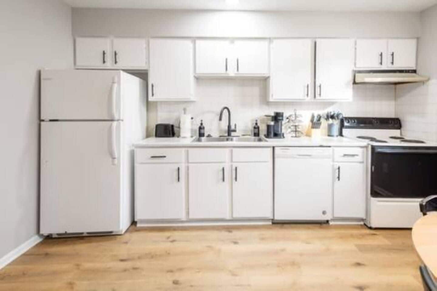 A kitchen with white cabinets, a refrigerator, a stove, and a sink.